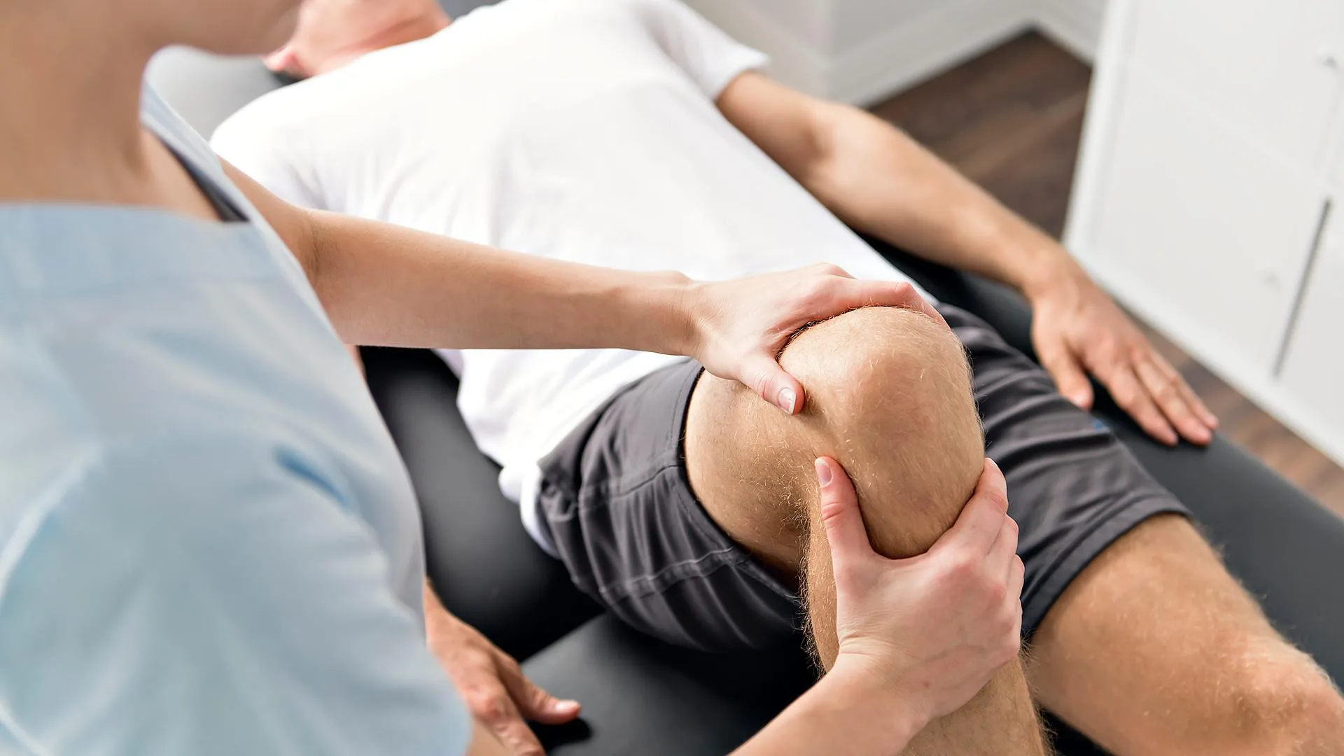 Physiotherapeutin behandelt das Knie eines liegenden Patienten