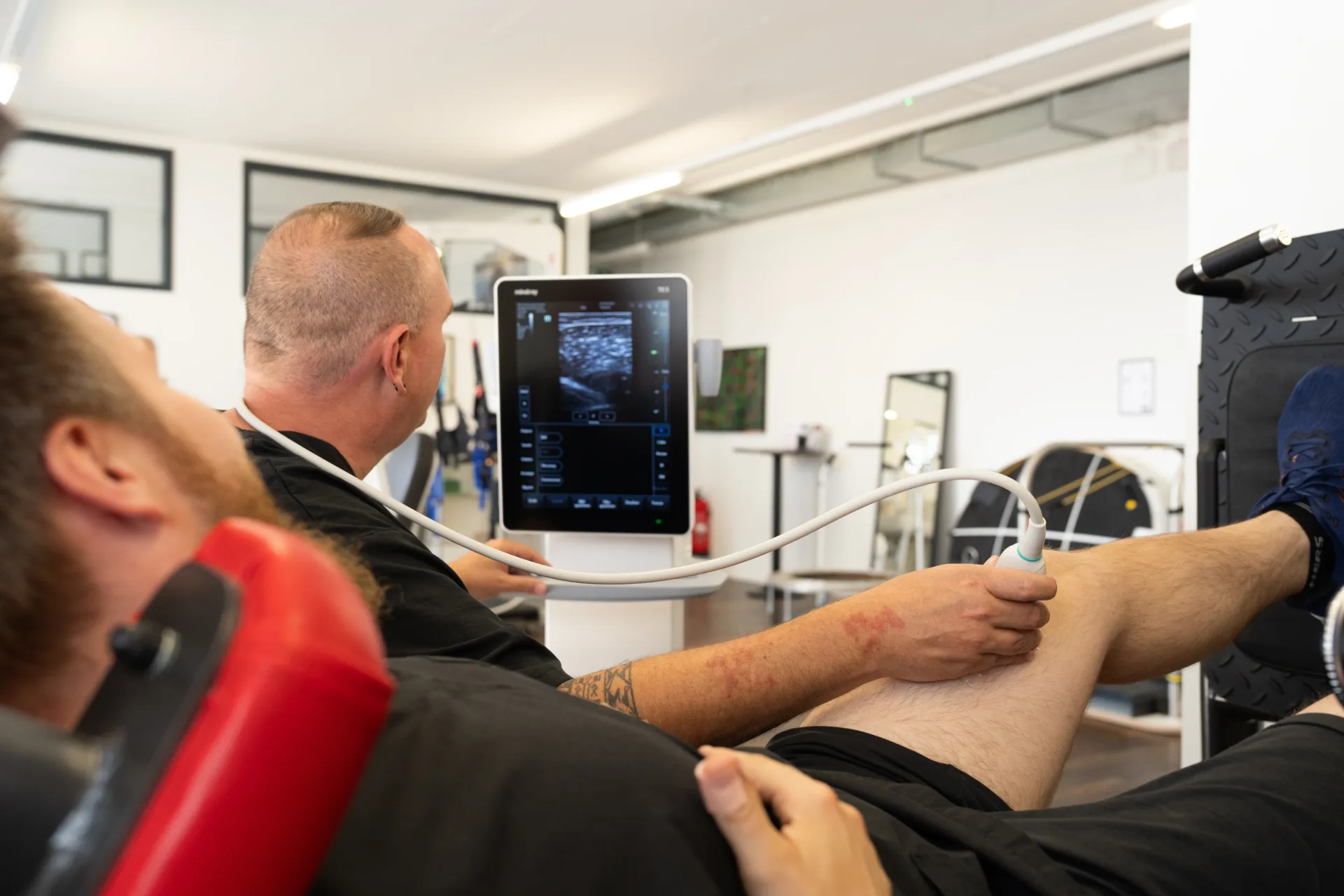 Patient auf der Behandlungsliege, Therapeut f&uuml;hrt eine Ultraschalluntersuchung am Bein durch