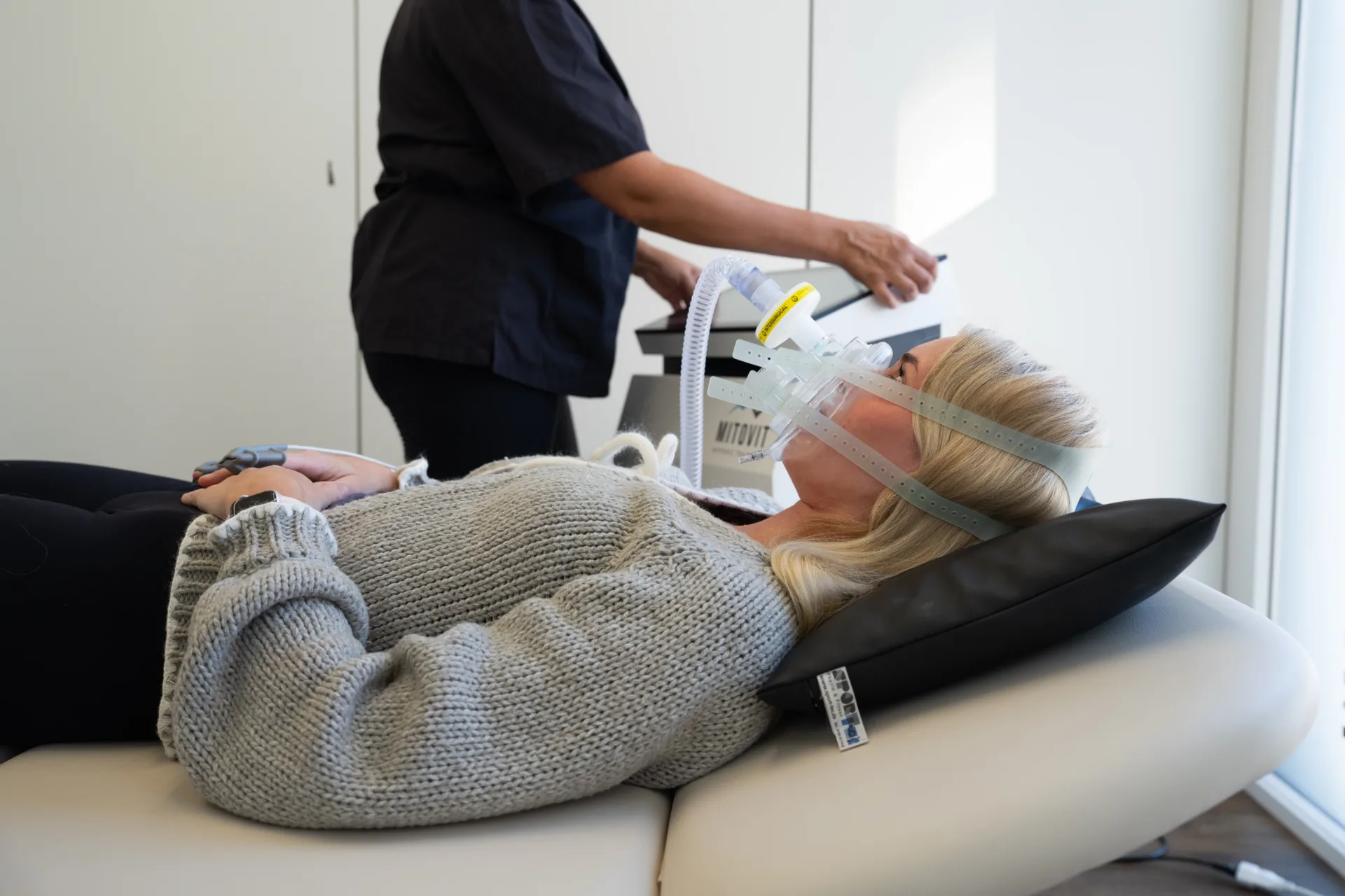 Patientin liegt mit Atemmaske auf der Liege, eine Therapeutin bedient das Ger&auml;t